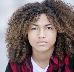 a close up of a person with curly hair wearing a red and black checkered shirt