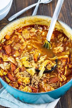 a blue pot filled with cabbage and meat soup on top of a wooden table next to silverware