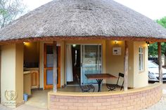 a small house with a thatched roof and table in the front yard, next to a car