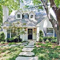 a white house that is surrounded by trees and grass in the front yard with stepping stones leading up to it