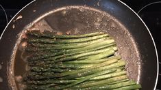 asparagus being cooked in a wok on the stove top with seasoning