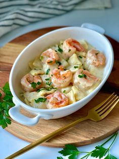 a bowl filled with pasta and shrimp on top of a wooden cutting board next to a fork