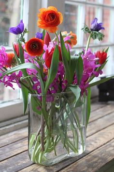 a vase filled with lots of colorful flowers on top of a wooden table next to a window