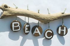 the word beach spelled with wooden letters hanging on a driftwood branch against a white wall