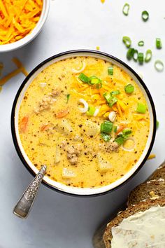 a bowl of soup with cheese, green onions and carrots next to a loaf of bread