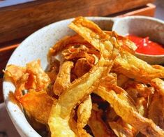 a white bowl filled with fried food and ketchup on top of a table