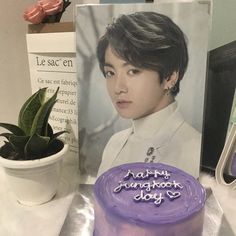 a purple cake sitting on top of a table next to a card and potted plant