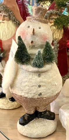 three snowmen with hats and trees on their heads are sitting in front of a christmas tree