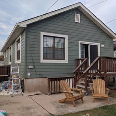 two wooden chairs sitting in front of a small gray house with stairs leading up to the second floor