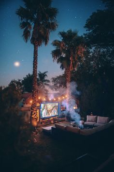 an outdoor movie theater with palm trees in the background and lights on at night time