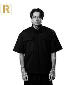 a man with tattoos standing in front of a white background wearing a black shirt and pants