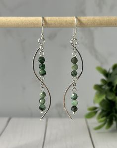 the earrings are made with green beads and silver wire, hanging from a wooden stick