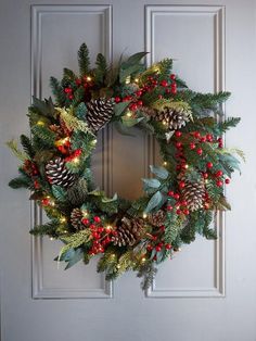 a christmas wreath with pine cones and red berries on the front door, lit by lights