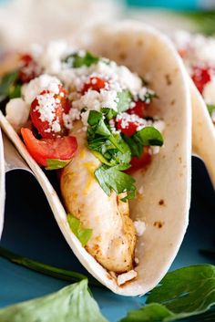 three tacos with meat, vegetables and cheese on them sitting on a blue plate