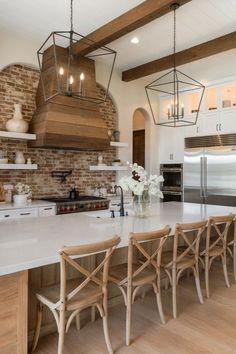 A modern kitchen with quartz countertops and a contrasting red brick backsplash. Countertops With Brick Backsplash, White Brick Kitchen, Exposed Brick Kitchen, Wooden Range, Wooden Range Hood, White Kitchen Countertops