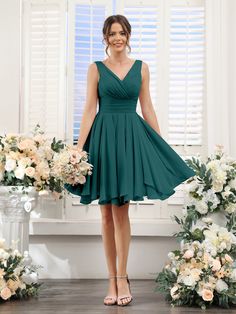 a woman in a short green dress standing next to flowers and greenery with her hands on her hips