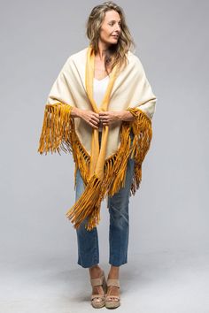 a woman wearing a yellow shawl with fringes on her arms and legs, standing in front of a gray background