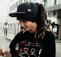 a woman with dreadlocks is looking at her cell phone while standing on the sidewalk