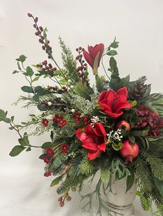 a white vase filled with red flowers and greenery