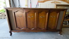 an old wooden cabinet in a garage with tools on the wall behind it and another piece of furniture next to it