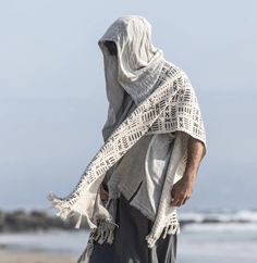 a person standing on the beach wearing a shawl and holding something in their hand