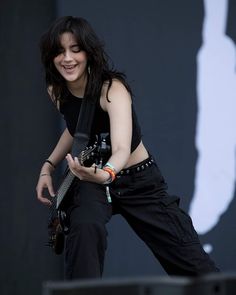 a woman with black hair playing an electric guitar on stage at a music festival or concert