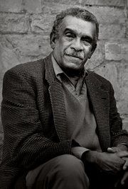 a black and white photo of a man sitting in front of a stone wall