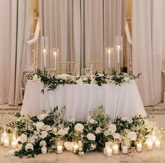 a table with candles, flowers and greenery is set up for a wedding reception