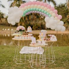 a table topped with cake and cupcakes under a rainbow arch