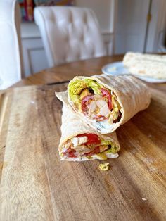 a burrito cut in half sitting on top of a wooden table next to a plate