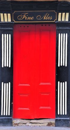 a red door with black and white trim in front of a brick building that says fine ales