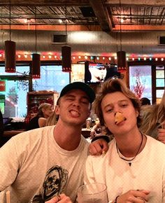 two young men sitting at a table with drinks and food in front of their faces