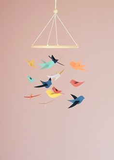 a mobile made out of paper birds hanging from a light fixture in a pink room