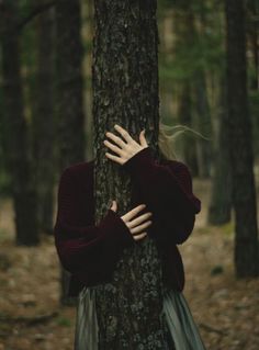 a woman is hugging a tree in the woods with her hands on it's face