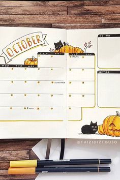 an open planner with cats and pumpkins on it, next to a pen and pencil