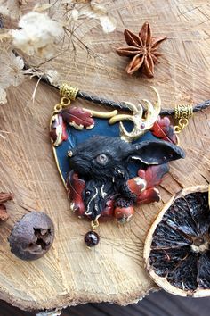 Fantastic designer necklace made of polymer clay. The Black Rabbit necklace decorated with Garnet stones and gold of leaf.  Straight from modern North American folktales comes the creature humorously called the Jackalope. The creature's name is a portmanteau merging the words "Jackrabbit" and "Antelope" to form the title "Jackalope." The Animal Ally's physical presence is such that it is among the modern-day chimeras, merging the features of two distinct beings in one body. In some stories, the Black Fantasy Necklace For Gift, Whimsical Black Necklace For Gift, Spiritual Polymer Clay Pendant Necklace, Spiritual Polymer Clay Necklaces For Gifts, Spiritual Polymer Clay Necklace As Gift, Nature-inspired Pendant Necklace With Hand Painted Details, Hand Painted Nature-inspired Pendant Necklace, Nature-inspired Hand Painted Pendant Necklace, Unique Gold Polymer Clay Jewelry