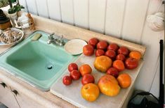 there are many tomatoes and oranges on the counter next to the sink in the kitchen