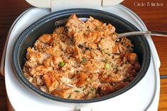 a bowl filled with rice and meat on top of a wooden table next to a fork