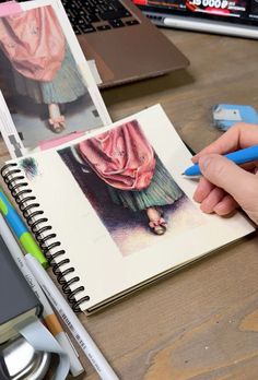 a person is holding a pencil and drawing pictures on a notebook next to a laptop