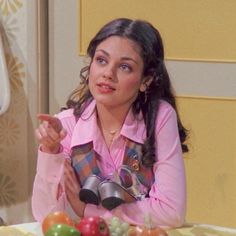 a woman sitting at a table with fruits and vegetables