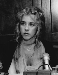 black and white photograph of a woman sitting at a table with a microphone in front of her