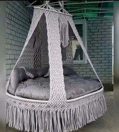 a bed made out of rope with pillows and fringes on the bottom, sitting in front of a brick wall