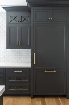 an image of a kitchen with black cabinets and white counter tops, gold pulls on the doors