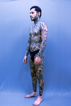 a man with tattoos on his body is standing in front of a blue background and posing for the camera