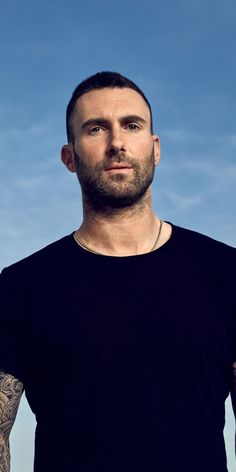 a man with tattoos standing in front of a blue sky