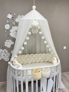 a white crib with flowers on the side and a canopy over it, in front of a gray wall