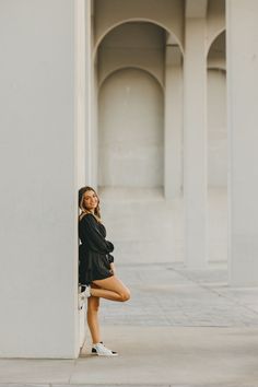 a woman leaning against a wall with her legs crossed