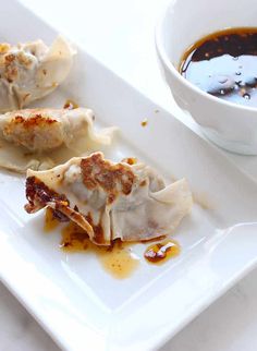 some dumplings are sitting on a white plate next to a bowl of dipping sauce