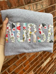 a person holding up a gray t - shirt with the word nurse printed on it