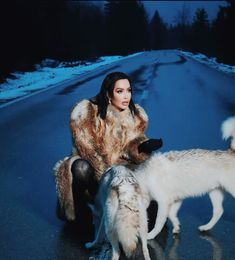 a woman sitting on the ground next to two dogs and one is wearing a fur coat